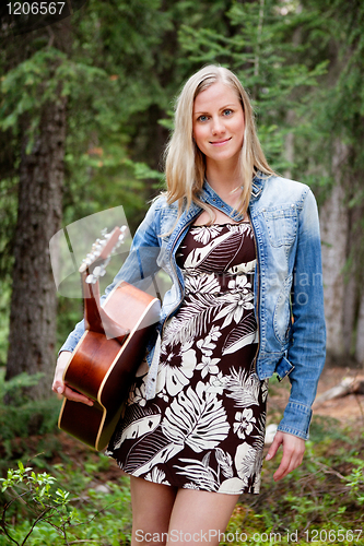 Image of Female holding guitar against trees