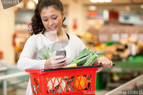 Image of Smiling woman using mobile phone in shopping store