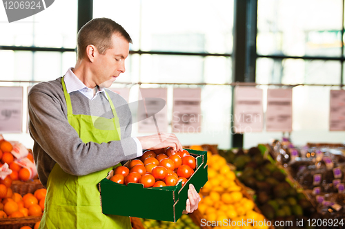 Image of Market assistant holding box of tomatoes