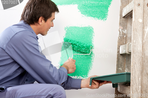 Image of Mature man painting the wall with a roller
