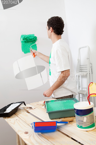 Image of Casual man painting the wall of his new apartment