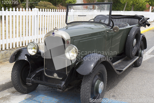 Image of Green convertible classic car parked near a white fence.