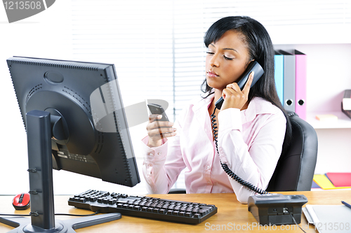 Image of Black businesswoman using two phones at desk