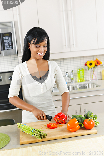 Image of Young woman cutting vegetables in kitchen