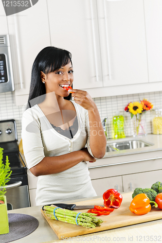 Image of Young woman tasting vegetables in kitchen