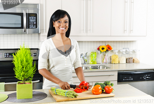 Image of Young woman cutting vegetables in kitchen