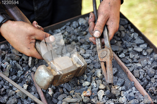 Image of Detail of dirty hands holding hammer and pliers - blacksmith