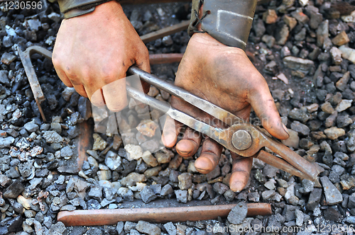 Image of Detail of dirty hands holding pliers - blacksmith