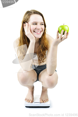 Image of Young smiling girl on bathroom scale holding apple