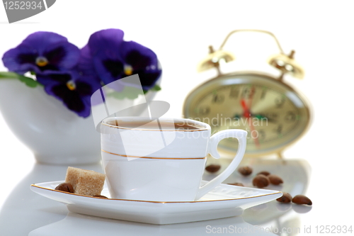 Image of A cup of coffee with a clock and a bouquet of flowers.