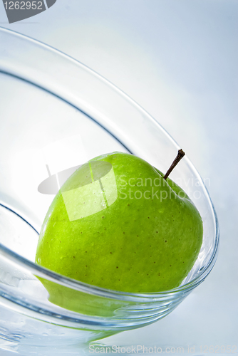 Image of green apple in glass plate on blue background