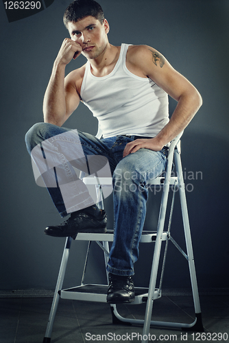 Image of attractive man in jeans sitting on stairs