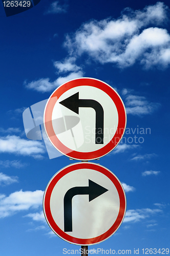 Image of two opposite road signs against blue sky and clouds