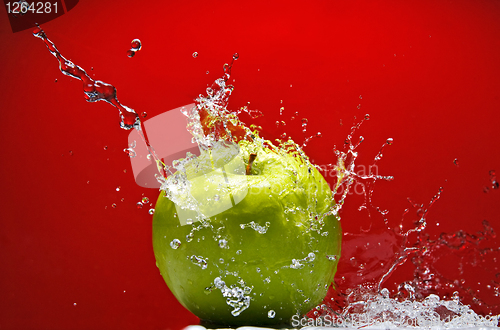 Image of Green apple with water splash on red background