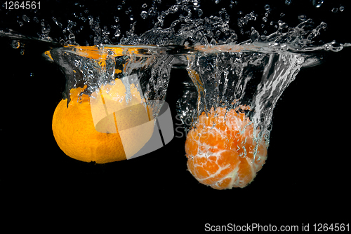 Image of Fresh tangerines dropped into water with bubbles on black