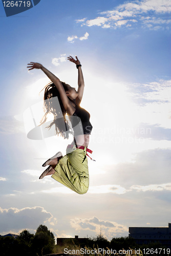 Image of A young girl jumping in front of blue sky and sun
