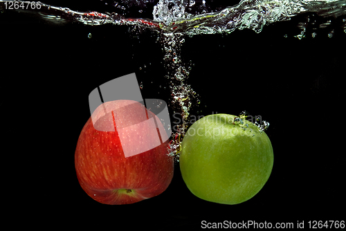 Image of ref and green apple dropped into water with splash isolated on b