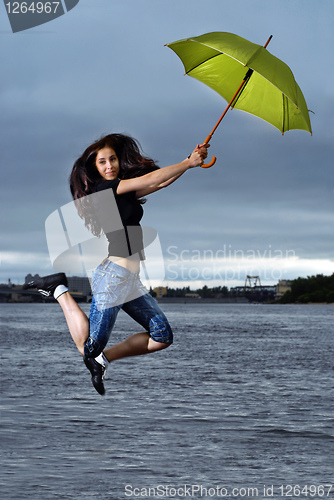 Image of girl jumping against sky and water with umbrella