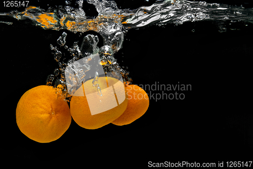 Image of Fresh tangerines dropped into water with bubbles on black