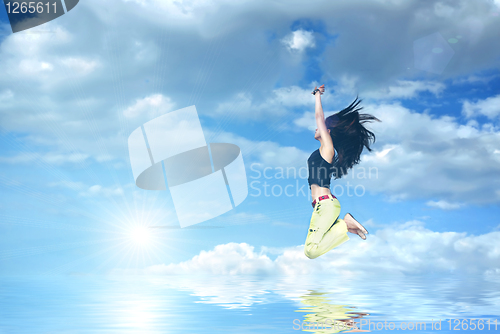 Image of girl jumping against blue sky and sun with water reflection