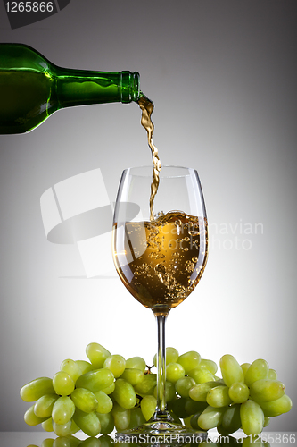 Image of White wine pouring into glass from bottle with green grape