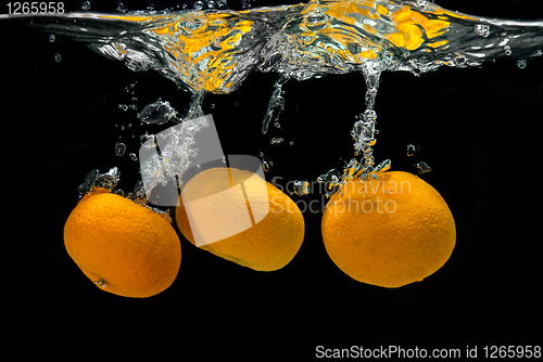 Image of Fresh tangerines dropped into water with bubbles on black