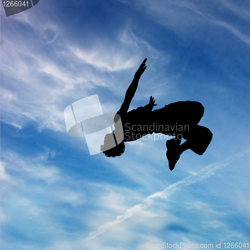 Image of silhouette of jumping man against blue sky and clouds