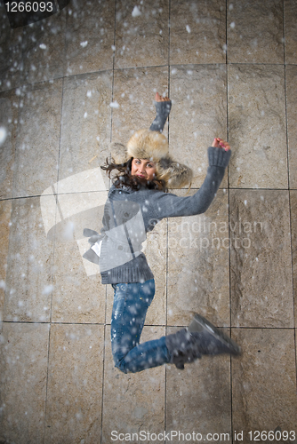 Image of young woman jumping in fur hat against the wall