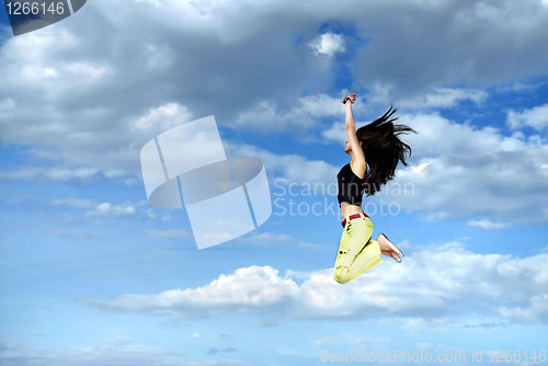 Image of A young girl jumping in front of blue sky and clouds