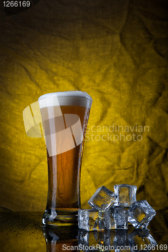 Image of Beer in glass with ice cubes on yellow background