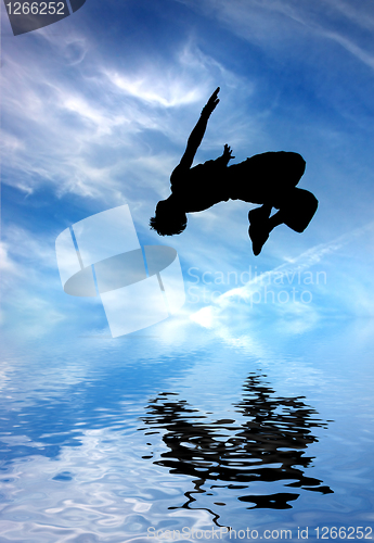 Image of silhouette of jumping man against blue sky and clouds