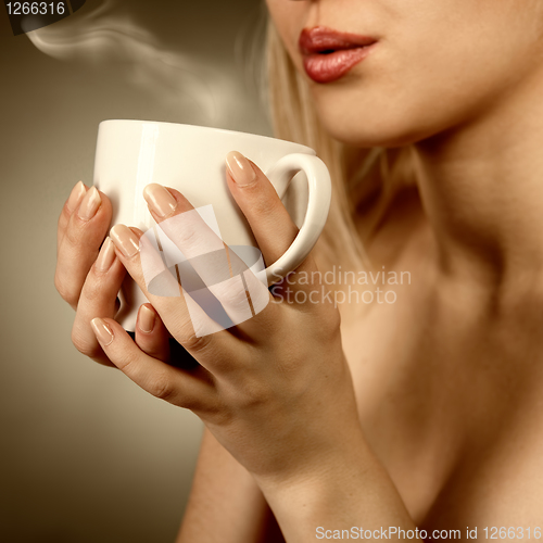 Image of woman holding hot cup and blowing on it
