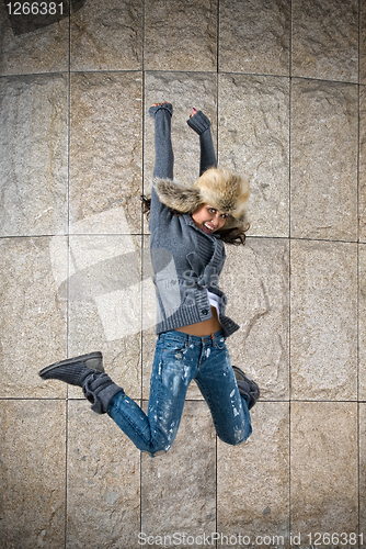 Image of young woman jumping in fur hat against the wall