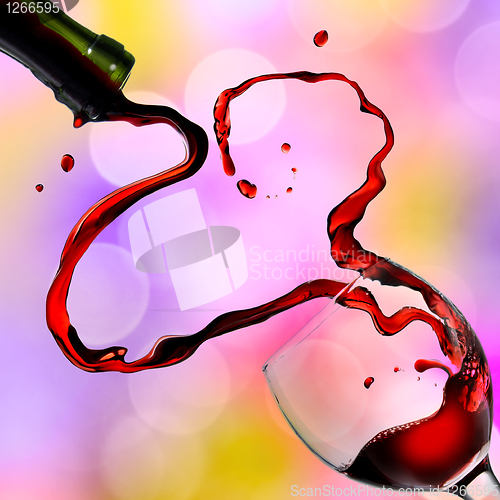 Image of Heart from pouring red wine in goblet on color background