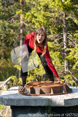 Image of Woman tries to lift rusty manhole