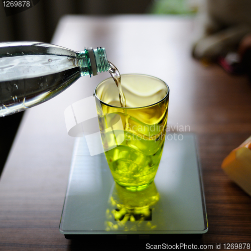Image of Bottle pouring water into a glass against kitchen background