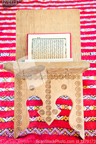 Image of Warsh quran open on a wooden stand on a red Moroccan rug