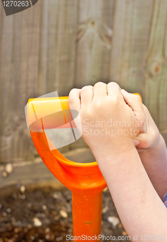 Image of Young child's hands holding the hanÉdle of a gardening spade