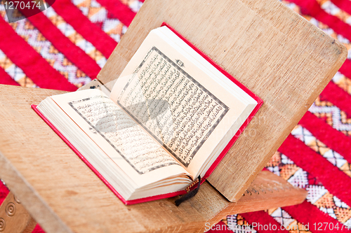 Image of Warsh quran open on a wooden stand on a red Moroccan rug