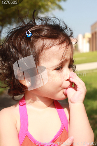 Image of Little baby girl, sucking her thumb walking in the park