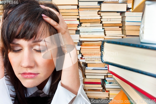 Image of College girl holding her head against many books