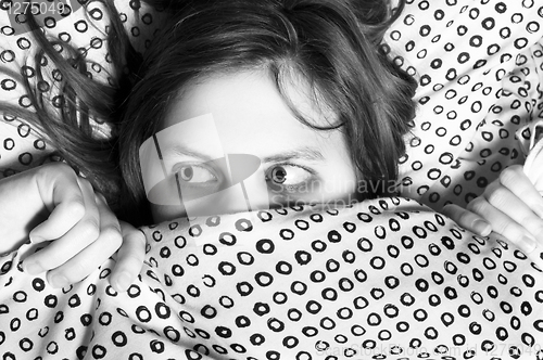 Image of Young scared girl hiding under blanket