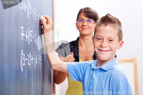 Image of Boy standing on chalkboard in front of teacher