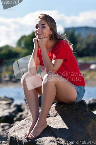 Image of girl in a red sweater sits on a rock