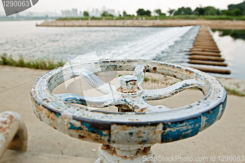 Image of White and blue rusty industrial faucet wheel on river blurry bac