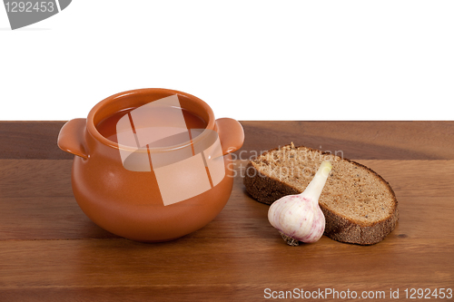 Image of Borsch in ceramic pot with bread and garlic on wooden table