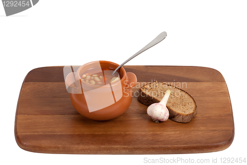 Image of Soup in clay pot with bread and garlic on wooden kitchen board.