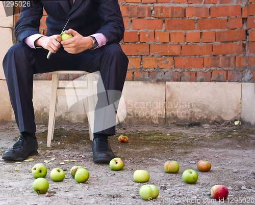 Image of Businessman cleaning apples sitting on a stool