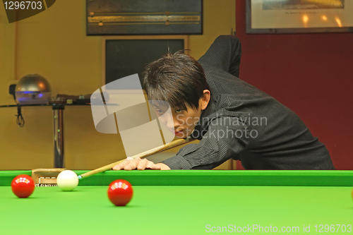 Image of Young man concentrating while aiming at pool ball while playing 