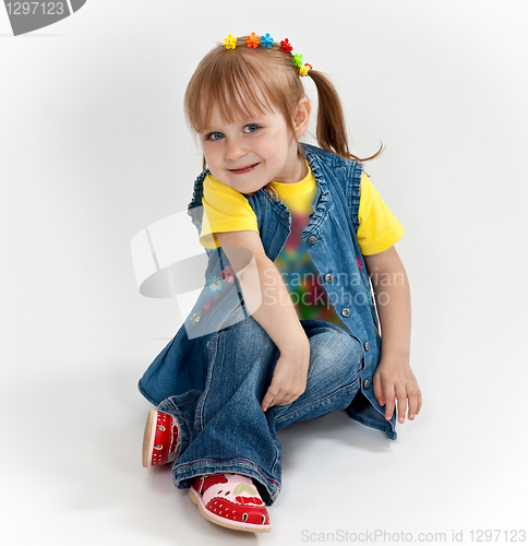 Image of little girl in jeans and sandals is sitting on the floor